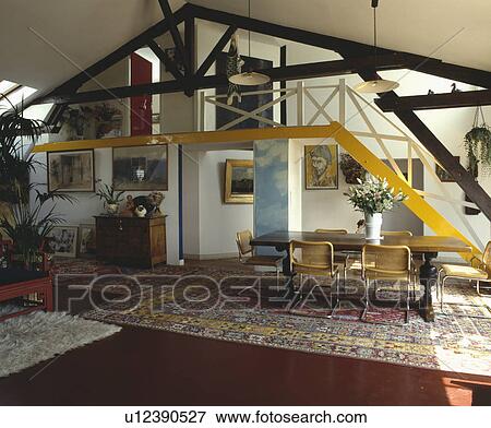 Chrome and cane chairs and rectangular table in modern hall dining room with yellow metal staircse and oriental rugs View Large Photo Image Stock Photo - Chrome and cane chairs and rectangular table in modern hall dining room with yellow metal staircse and oriental rugs. Fotosearch