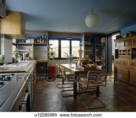 Chrome and cane chairs and wooden table in pastel blue kitchen with terracotta floor tiles View Large Photo Image Stock Photography - Chrome and cane chairs and wooden table in pastel blue kitchen with terracotta floor tiles. Fotosearch