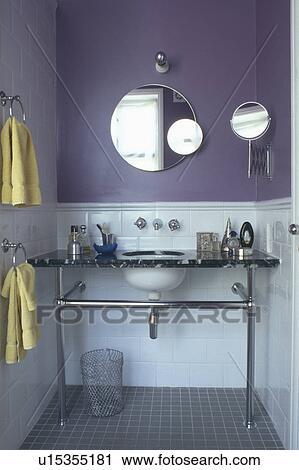 Stock Image - Circular mirrors on wall above white basin in chrome vanity unit in purple clockroom with white tiled wall to dado height. Fotosearch