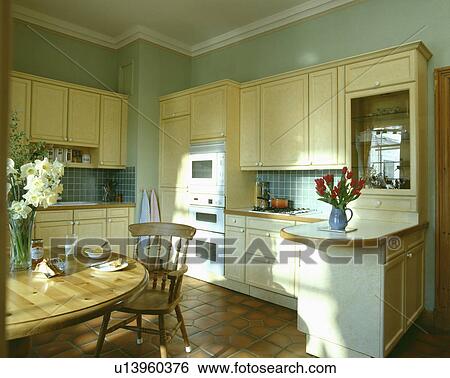 Circular pine table and chairs in pastel green country kitchen with cream fitted cupboards and units View Large Photo Image Stock Photograph - Circular pine table and chairs in pastel green country kitchen with cream fitted cupboards and units. Fotosearch