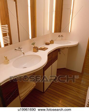 Circular whiite underset basins in moulded curved vanity unit in contemporary mirrored bathroom with wooden floor View Large Photo Image Stock Image - Circular whiite underset basins in moulded curved vanity unit in contemporary mirrored bathroom with wooden floor . Fotosearch