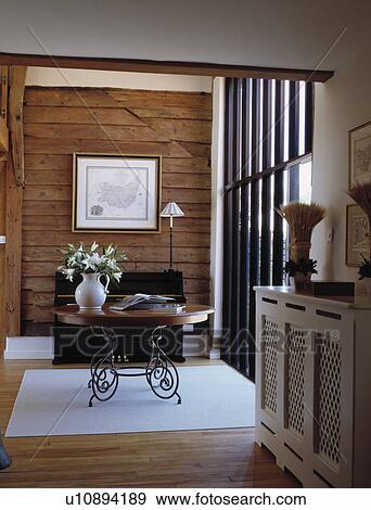 Circular wood table with metal legs in barn conversion hall with wood panelled wall and white fretwork radiator cover View Large Photo Image Stock Photo - Circular wood table with metal legs in barn conversion hall with wood panelled wall and white fretwork radiator cover. Fotosearch