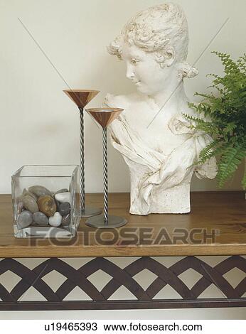Stock Image - Classical bust and metal candlesticks on shelf with pebbles in square glass vase . Fotosearch
