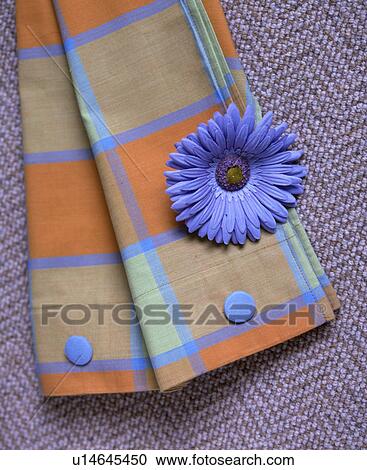 Stock Image - Close-up of blue plastic flower on orange+blue checked serviette. Fotosearch