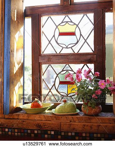 Stock Image - Close-up of Carltonware dishes and pot of pink daisies on windowsill below stained glass window. Fotosearch