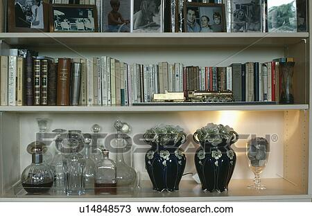 Stock Image - Close-up of collection of glass decanters and black vases on bookshelves. Fotosearch