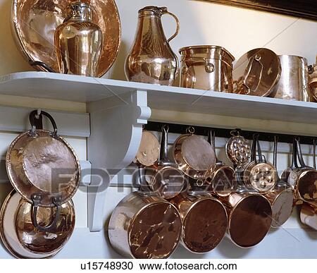 Stock Image - Close-up of copper pans and jugs on white shelf. Fotosearch