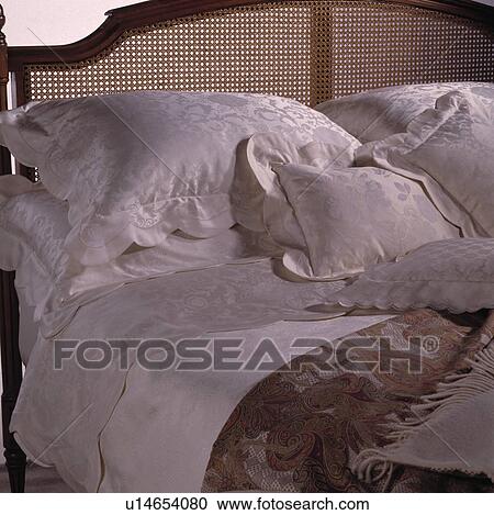 Stock Image - Close-up of cream damask pillows and sheet on Bergere bed. Fotosearch