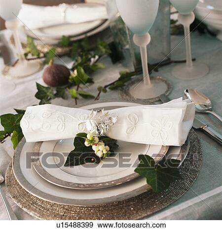 Stock Photo - Close-up of cream linen napkin on pewter-edged plates on Christmas table decorated with ivy leaves . Fotosearch