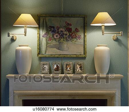 Picture - Close-up of lighted wall lights and picture above mantelpiece with white vases. Fotosearch