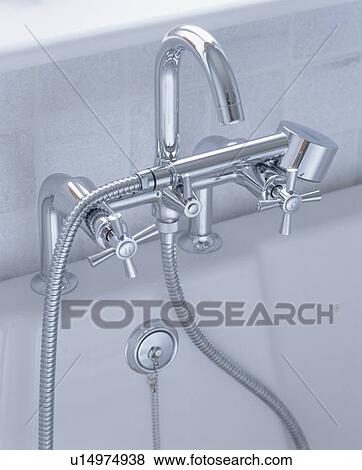 Stock Photo - Close-up of modern chrome taps and shower head in white bath. Fotosearch