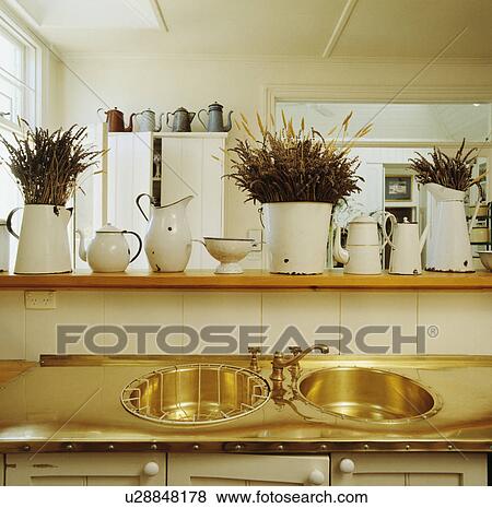 Close-up of old white enamel jugs on shelf above brass double circular sinks and draining board View Large Photo Image Stock Photo - Close-up of old white enamel jugs on shelf above brass double circular sinks and draining board. Fotosearch