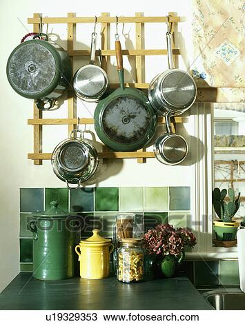 Stock Image - Close-up of pans hanging from wooden wall-rack above green tiles in kitchen. Fotosearch