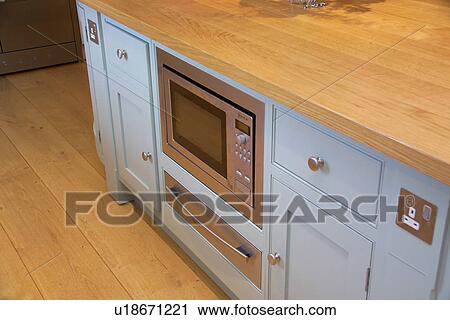 Stock Image - Close-up of pastel blue kitchen unit with fitted microwave oven and electric plug socket. Fotosearch