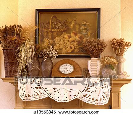 Stock Photography - Close-up of picture above mantelpiece with clock and dried flowers in vases. Fotosearch