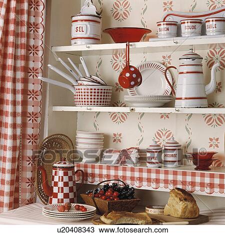 Stock Image - Close-up of red+white pots and coffeepot with crockery on white shelves beside red+white checked curtains. Fotosearch