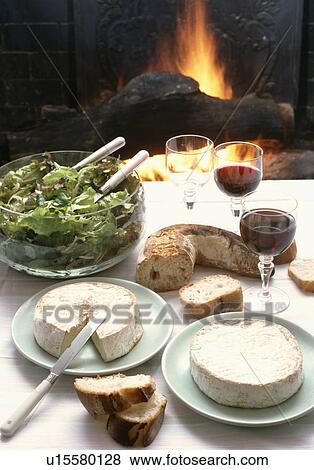 Stock Photo - Close up of salad and selection of cheeses on table in front of the fire. Fotosearch