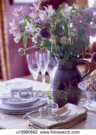 Stock Image - Close-up of settings fresh flowers in pottery jug on dining table. Fotosearch