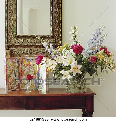 Close-up of small picture and summer flowers in informal arrangement in glass vase on table below ornate mirror View Large Photo Image Stock Photo - Close-up of small picture and summer flowers in informal arrangement in glass vase on table below ornate mirror. Fotosearch