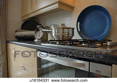 Stock Image - Close-up of stainless steel pan on gas hob with circular blue tray at the back. Fotosearch