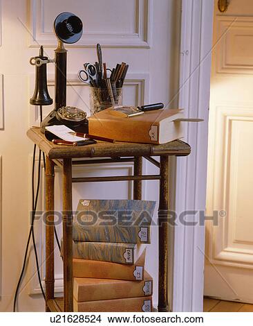 Picture - Close-up of thirties telephone on old bamboo table with pile of books. Fotosearch