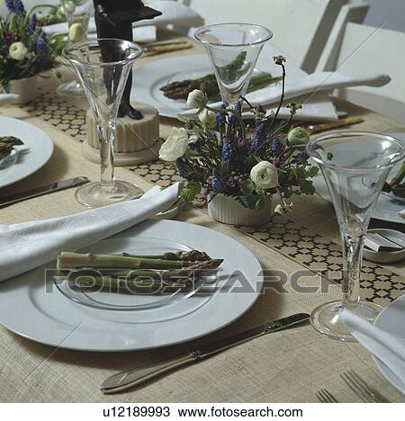 Stock Image - Close up of wineglasses and asparagus on white plates on beige linen tablecloth. Fotosearch