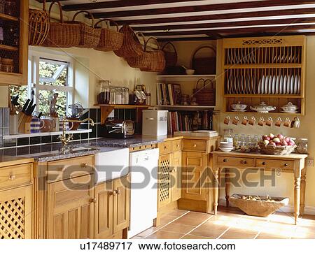Stock Photo - Collection of baskets on ceiling above sink and dishwasher in wooden cottage kitchen with plate rack above side table. Fotosearch