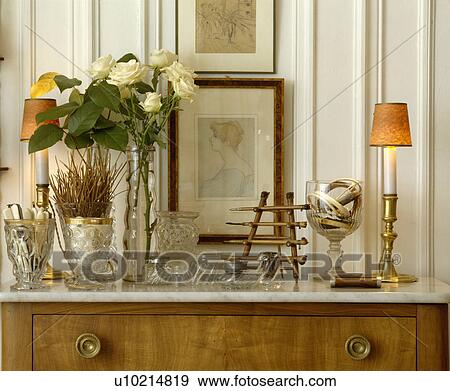 Stock Photo - Collection of pressed glass vases and cream roses with pictures and lighted lamp. Fotosearch