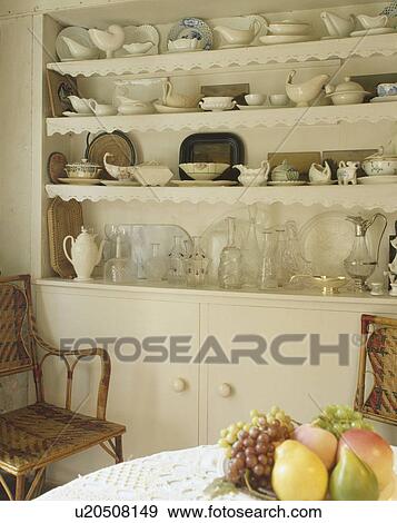 Collection of white china and glasses on white shelves with trimmings in traditional dining room View Large Photo Image Stock Photo - Collection of white china and glasses on white shelves with trimmings in traditional dining room. Fotosearch