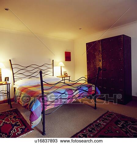Colourful patchwork duvet on modern wrought-iron bed in bedroom with large wardrobe View Large Photo Image Stock Image - Colourful patchwork duvet on modern wrought-iron bed in bedroom with large wardrobe. Fotosearch