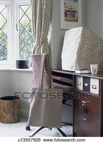 Stock Photograph - Computer with striped cover on desk in homeoffice with shopping bag on chair. Fotosearch
