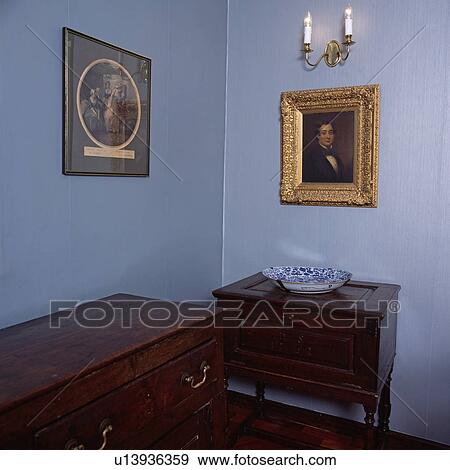 Stock Photo - Corner of blue room with paintings above antique cupboard and chest of drawers. Fotosearch