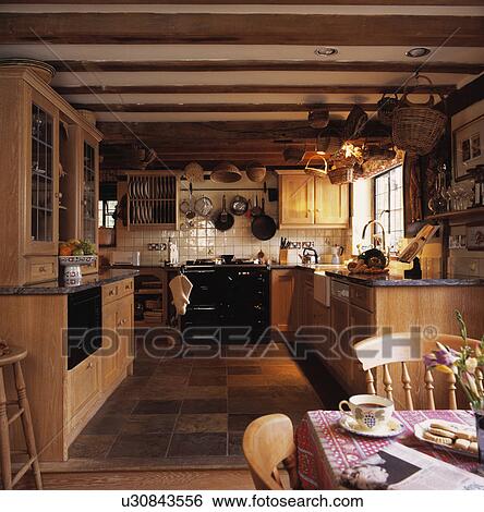 Stock Photograph - Country kitchen with wooden fitted cupboards and black Aga. Fotosearch
