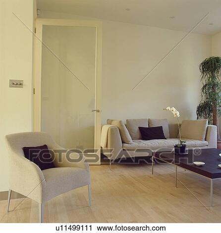 Stock Image - Cream armchair and sofa in modern livingroom with maple wood flooring and glass door. Fotosearch