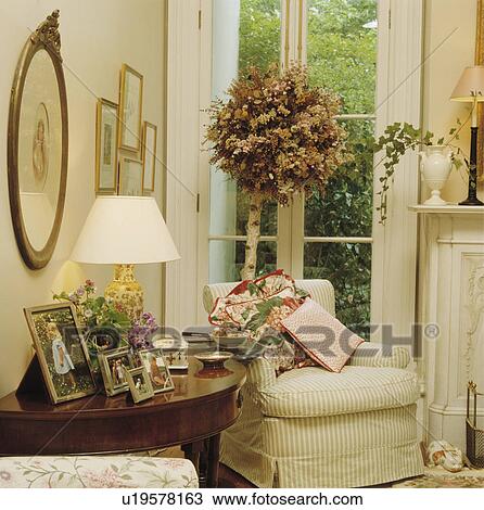 Cream loosecover on armchair in front of dried flower tree in traditional living room View Large Photo Image Stock Image - Cream loosecover on armchair in front of dried flower tree in traditional living room. Fotosearch