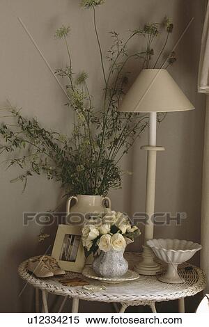 Stock Photography - Cream roses in vase and cream lamp with small pair of cream shoes on circular cream table. Fotosearch