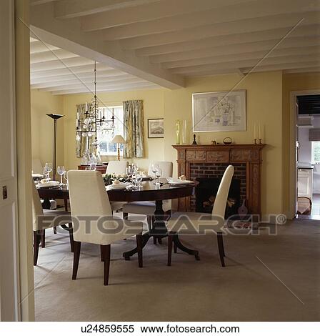 Stock Photography - Cream upholstered chairs and antique table in pastel yellow country dining room with white beamed ceiling . Fotosearch