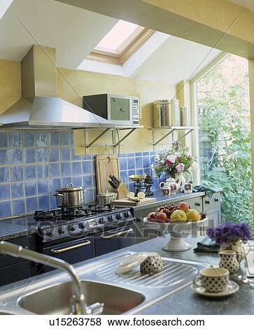 Crockery beside stainless steel sink in modern kitchen extension with blue wall tiles above range oven View Large Photo Image Stock Photo - Crockery beside stainless steel sink in modern kitchen extension with blue wall tiles above range oven. Fotosearch