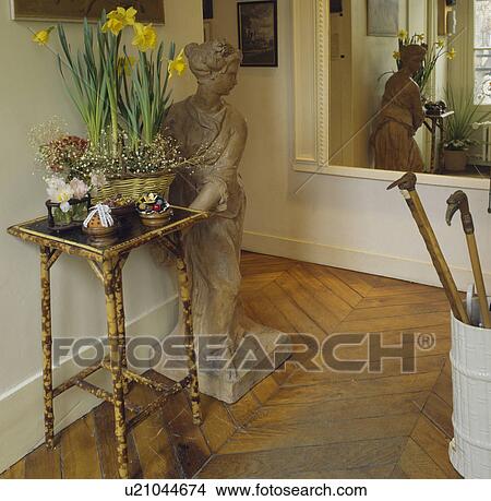 Picture - Daffodils in pot on bamboo table beside classical statue in white hall with large mirror and parquet flooring. Fotosearch