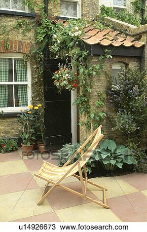 Stock Image - Deckchair on paving in front of traditional house in the country. Fotosearch