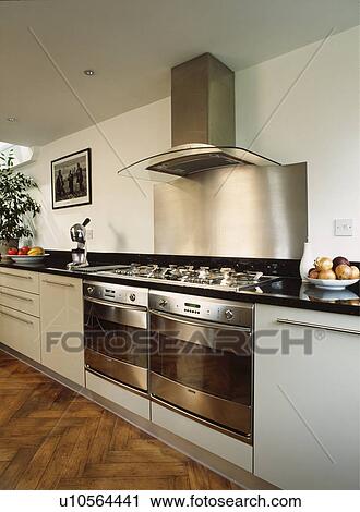 Stock Image - Detail of contemporary cream kitchen with stainless steel built in double cooker and hood and parquet flooring. Fotosearch
