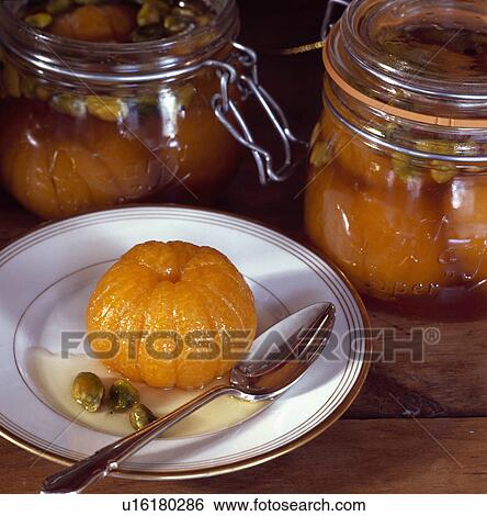 Stock Photograph - Detail of preserving jars, whole preserved mandarin orange in syrup with nuts on a white plate . Fotosearch