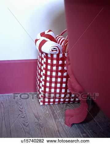 Stock Image - Detail of red and white check bag of towels against free standing claw foot bath. Fotosearch
