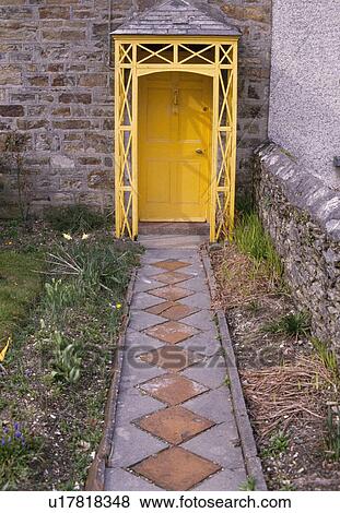 Stock Photo - Diamond patterned paving in path to yellow front door with ornate wooden porch. Fotosearch