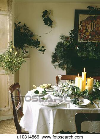 Dining room at Christmas with natural decorations of holly and ivy with candles on table with white cloth and plates View Large Photo Image Stock Photograph - Dining room at Christmas with natural decorations of holly and ivy with candles on table with white cloth and plates. Fotosearch
