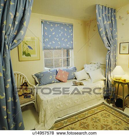 Stock Photo - Divan bed with crochet cover in front of butterfly-patterned blue blind at window and matching curtains screening bed. Fotosearch