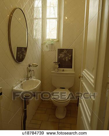 Stock Photo - Door open to basin and toilet in small white tiled cloakroom. Fotosearch