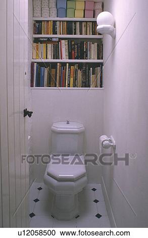 Stock Image - Door open to books on shelves above modern toilet in small white cloakroom. Fotosearch
