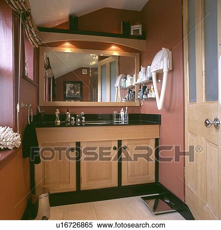 Stock Photography - Downlighters above mirror in small terracotta bathroom with hairdryer on the wall. Fotosearch