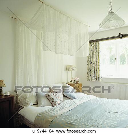 Draped voile panel above bed in with pale blue linen and cushions in small white bedrooms View Large Photo Image Picture - Draped voile panel above bed in with pale blue linen and cushions in small white bedrooms. Fotosearch